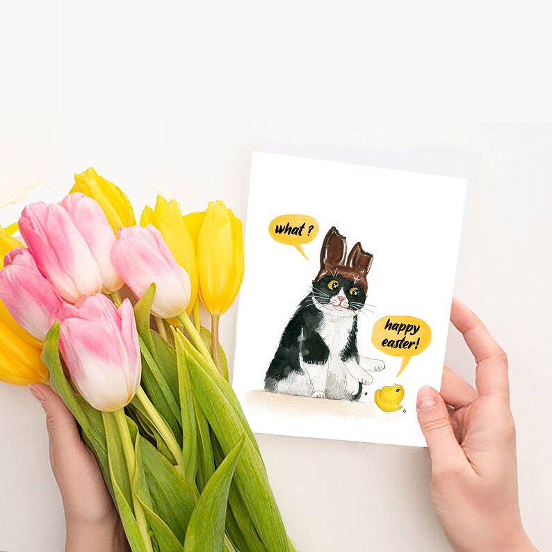 May include: A greeting card featuring a black and white cat with brown bunny ears. The cat is looking at a small yellow chick with a speech bubble that says "happy easter!" The cat has a speech bubble that says "what?"