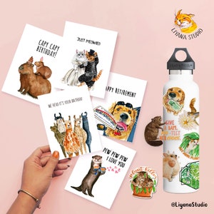 Pu&ograve; includere: Una collezione di biglietti di auguri e adesivi ad acquerello con illustrazioni di animali. I biglietti contengono frasi come "Capy Capy Birthday!" e "Just Meowied". &Egrave; visibile anche una borraccia Hydro Flask bianca, decorata con adesivi a tema animale.