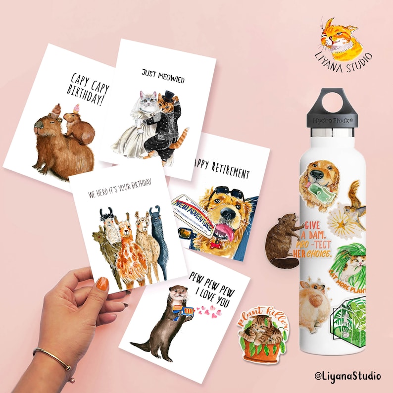 Pu&ograve; includere: Una collezione di biglietti di auguri e adesivi ad acquerello con illustrazioni di animali. I biglietti contengono frasi come "Capy Capy Birthday!" e "Just Meowied". &Egrave; visibile anche una borraccia Hydro Flask bianca, decorata con adesivi a tema animale.