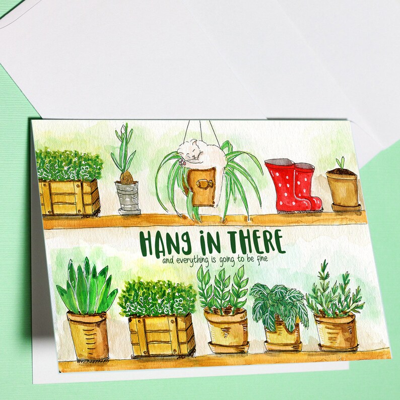 Peut inclure: Une illustration aquarelle d'une carte de v&oelig;ux avec le texte "Hang in there and everything is going to be fine". La carte pr&eacute;sente une vari&eacute;t&eacute; de plantes en pot et un chat dormant dans une jardini&egrave;re suspendue.