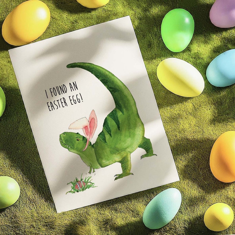 May include: A green dinosaur with pink bunny ears holds an Easter egg. The dinosaur is on a white card with the text "I found an Easter egg!"
