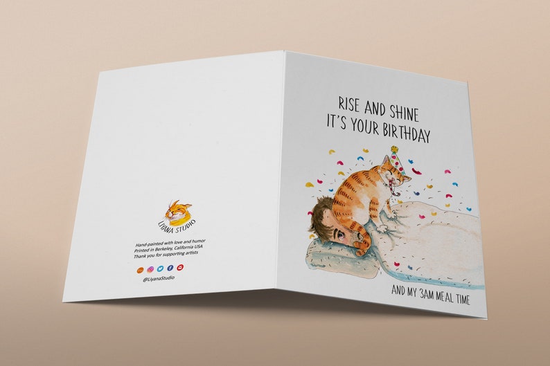 May include: A greeting card featuring a watercolour illustration of a cat wearing a party hat, waking someone up. The text on the card reads "Rise and shine it's your birthday and my 3am meal time."