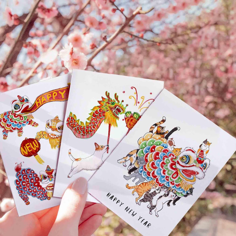 May include: Three greeting cards with colorful illustrations of Chinese New Year themes. One card features a lion dance with the word "HAPPY" on a banner. Another shows a dragon, and the third depicts a lion dance with cats. The words "HAPPY NEW YEAR" are printed on the bottom.
