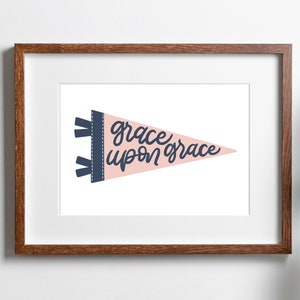 May include: A framed print of a pink pennant with the text "grace upon grace" in navy blue cursive lettering.