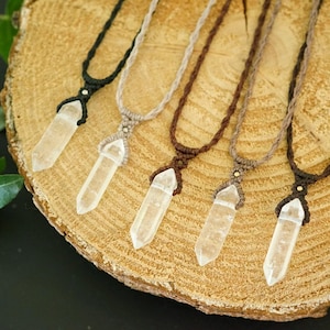 Peut inclure: Cinq colliers avec des pendentifs en cristal transparent, hexagonal et pointu, suspendus à des cordons tressés de couleur noire, beige clair, marron foncé, beige et marron. Chaque pendentif est fixé par un nœud macramé et une perle métallique.