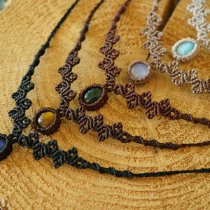 Puede incluir: Cuatro collares con intrincados cordones de macram&eacute; en negro, marr&oacute;n oscuro, marr&oacute;n medio y beige. Cada collar se centra en una sola piedra preciosa ovalada, incluyendo piedras azules, ojo de tigre, verde oscuro, azul claro y blanco iridiscente.
