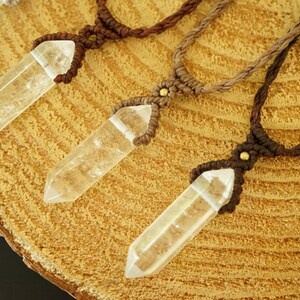 May include: Three necklaces featuring clear, faceted, hexagonal crystal points suspended from braided cord. Each pendant is secured with a macrame knot and a small, round, metallic bead. The cords vary in shades of brown, from light tan to dark brown.