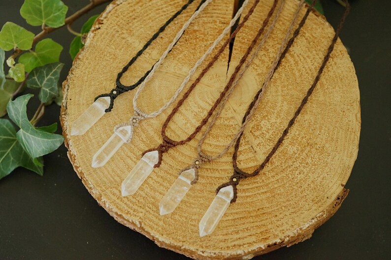 May include: Five necklaces featuring clear, pointed crystal pendants suspended on woven cord. The cords are available in black, beige, and various shades of brown, each secured with a small bead above the crystal point for a secure fit.