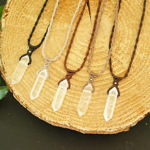 May include: Five necklaces featuring clear, pointed crystal pendants suspended on woven cord in black, beige, dark brown, light brown, and medium brown. Each pendant is secured with a macrame-style knot and a small bead at the top of the crystal.
