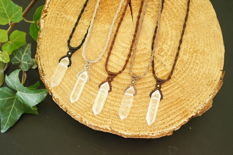 May include: Five necklaces featuring clear, pointed crystal pendants suspended on woven cord in black, beige, dark brown, light brown, and medium brown. Each pendant is secured with a macrame-style knot and a small bead at the top of the crystal.
