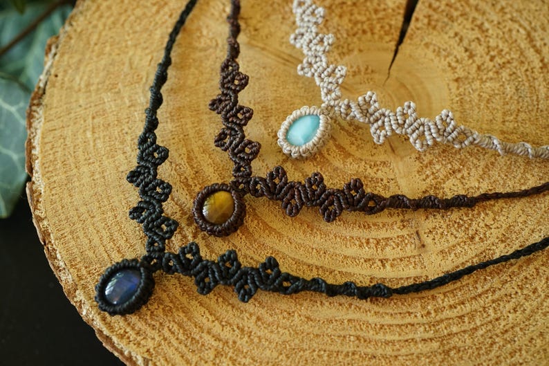 Puede incluir: Tres collares de macram&eacute; con intrincados patrones de cord&oacute;n anudado en negro, marr&oacute;n oscuro y beige. Cada collar est&aacute; centrado con una piedra preciosa ovalada pulida, incluyendo una piedra azul oscuro, un ojo de tigre marr&oacute;n dorado y una azul claro.