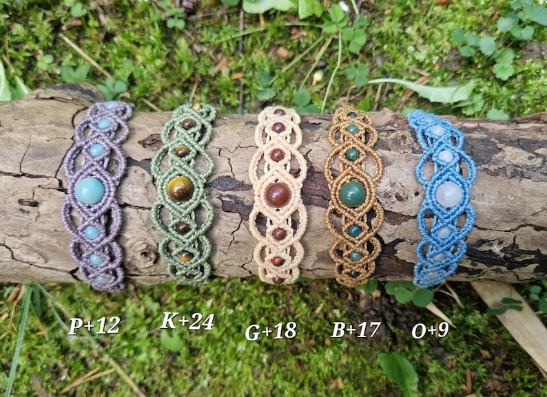 Puede incluir: Cinco pulseras de macram&eacute; con detalles de piedras preciosas en varios colores, incluyendo morado, verde, beige y azul. Cada pulsera presenta una piedra preciosa &uacute;nica y se exhibe sobre un tronco de madera. Las pulseras est&aacute;n etiquetadas con letras y n&uacute;meros.
