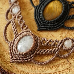 May include: Close-up of three macrame necklaces. The necklaces are brown and black, with oval and round gemstones. The brown necklace has a large oval gemstone in the center and smaller round gemstones. The black necklace has a large oval gemstone.