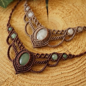 May include: Two handmade macrame necklaces with gemstone accents. One necklace features a large oval green stone and smaller green beads, while the other has a large oval white stone and smaller white beads. Both are brown.