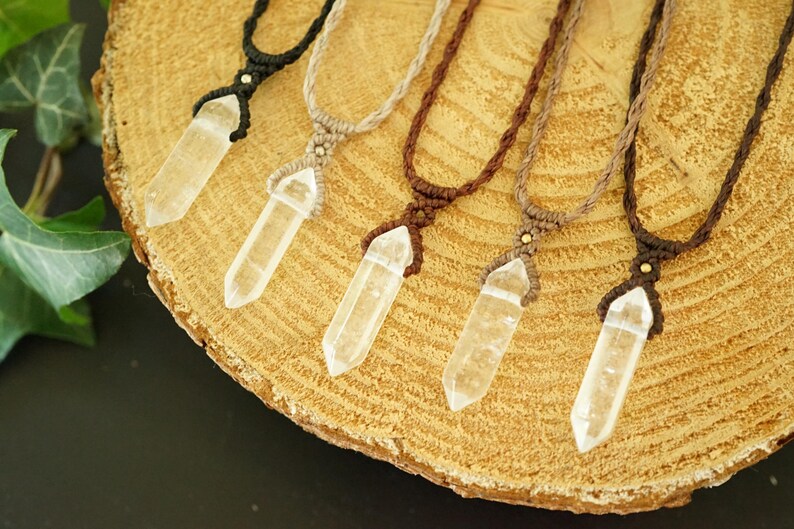 May include: Five necklaces featuring clear, faceted crystal points suspended from macrame cords in black, beige, dark brown, light brown, and deep brown. Each pendant is secured with a small metallic bead at the top of the woven cord setting.