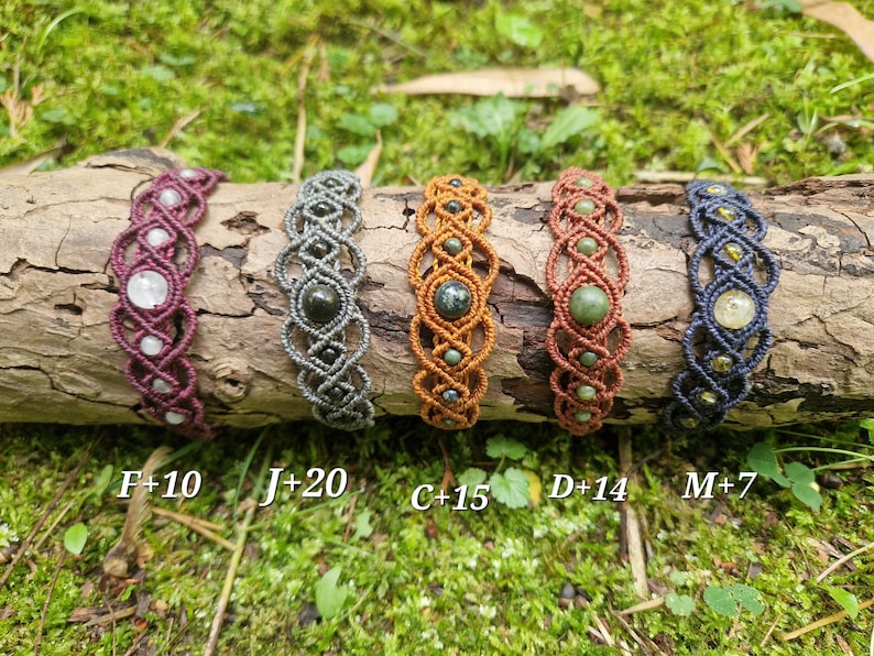 Puede incluir: Cinco pulseras de macram&eacute; con detalles de piedras preciosas se exhiben sobre un tronco. Las pulseras var&iacute;an en color, incluyendo burdeos, gris, naranja, marr&oacute;n y azul marino. Cada pulsera presenta una combinaci&oacute;n &uacute;nica de piedras preciosas y nudos.