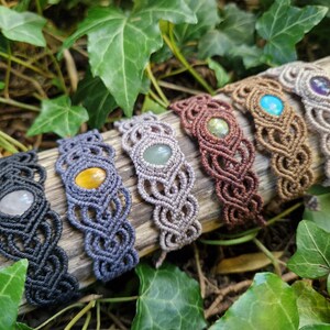May include: A collection of six macrame bracelets with gemstone accents. The bracelets are in various colors, including black, gray, brown, and tan. Each bracelet features a different gemstone, such as quartz, tiger's eye, and turquoise.