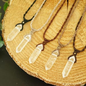 May include: Five necklaces featuring clear, pointed crystal pendants suspended from woven cords in black, beige, and various shades of brown. Each pendant is secured with a knotted cord design and a small metallic bead accent at the top.