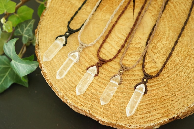 May include: Five necklaces featuring clear, pointed crystal pendants suspended from woven cords in black, beige, and various shades of brown. Each pendant is secured with a knotted cord design and a small metallic bead accent at the top.