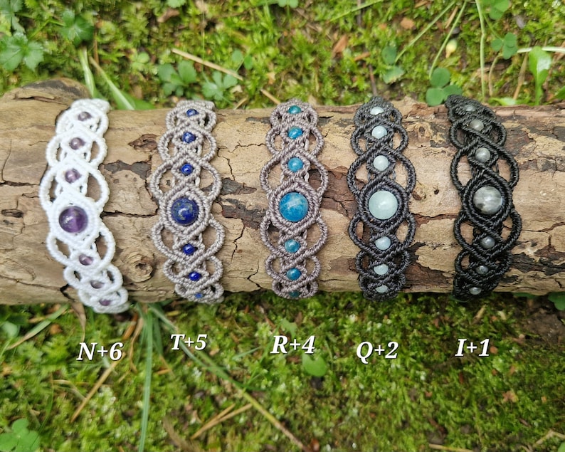 Puede incluir: Cinco pulseras de macram&eacute; con piedras preciosas, incluyendo amatista, lapisl&aacute;zuli y turquesa, se exhiben sobre un tronco de madera. Las pulseras son de cordones blancos, grises y negros. Cada pulsera tiene una disposici&oacute;n &uacute;nica de piedras preciosas. El texto "N+6", "T+5", "R+4", "Q+2" e "I+1" es visible.