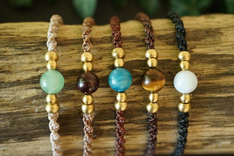 May include: Five handmade bracelets with different colored beads and gold-colored accents. The beads are green, brown, blue, tiger's eye, and white. The bracelets are strung on braided cords in various colors.
