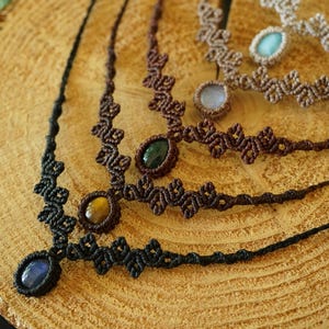 Puede incluir: Cuatro collares de macram&eacute; con dise&ntilde;os de cord&oacute;n anudado en negro, marr&oacute;n oscuro y beige. Cada collar presenta una piedra preciosa ovalada central, incluyendo piedras azules, ojo de tigre, verde oscuro y azul claro, en forma de V.