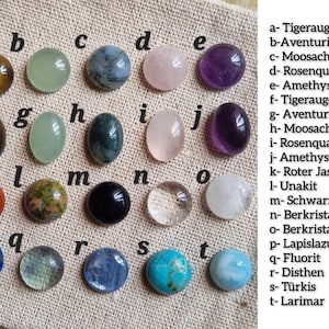 Puede incluir: Una colecci&oacute;n de veinte piedras preciosas pulidas dispuestas en una cuadr&iacute;cula, etiquetadas de la a a la t. Las piedras incluyen ojo de tigre, aventurina, &aacute;gata musgosa, cuarzo rosa, amatista, jaspe rojo, unakita, &aacute;gata negra, cuarzo claro, lapisl&aacute;zuli, fluorita, cianita, turquesa y larimar.