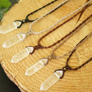 May include: Five necklaces featuring clear, pointed crystal pendants suspended on braided cords in varying shades of black, tan, and brown. Each pendant is secured with a knotted cord design, showcasing the natural transparency of the crystals.