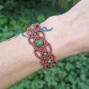 Puede incluir: Pulsera de macram&eacute; hecha a mano en color marr&oacute;n rojizo, con un dise&ntilde;o tejido y cuentas de piedras preciosas verdes. La pulsera se lleva en la mu&ntilde;eca. Las piedras preciosas miden unos 0,8 cm de di&aacute;metro.