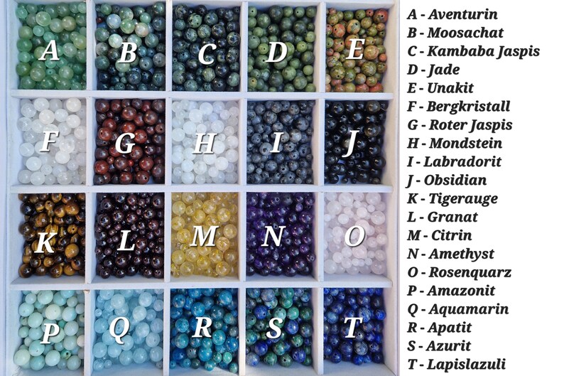 May include: A wooden tray filled with various gemstone beads, each in a separate compartment. The beads are in a variety of colors, including green, brown, white, black, yellow, purple, blue, and pink. Each compartment is labeled with a letter and a gemstone name.