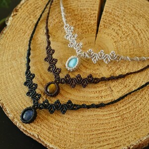 Puede incluir: Tres collares de macram&eacute; con intrincados dise&ntilde;os de cord&oacute;n anudado en negro, marr&oacute;n oscuro y beige. Cada collar est&aacute; centrado con un colgante de piedra preciosa pulida, incluyendo una piedra azul, un ojo de tigre y una piedra ovalada azul claro.