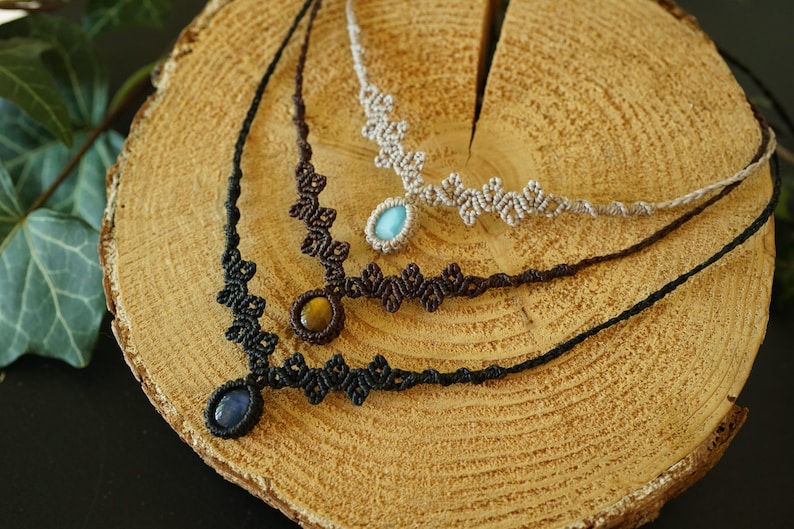 Puede incluir: Tres collares de macram&eacute; con intrincados dise&ntilde;os de cord&oacute;n anudado en negro, marr&oacute;n oscuro y beige. Cada collar est&aacute; centrado con un colgante de piedra preciosa pulida, incluyendo una piedra azul, un ojo de tigre y una piedra ovalada azul claro.