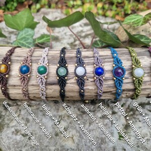 May include: A collection of handmade macrame bracelets, each featuring a central gemstone and gold-colored beads. The bracelets are in various colors, including brown, beige, black, gray, blue, green, and purple, with gemstones like tiger's eye, apatite, malachite, aventurine, moonstone, lapis lazuli, amethyst, and jade.