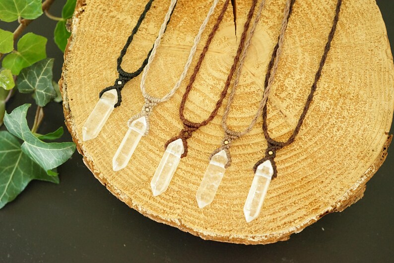 May include: Five necklaces featuring clear, hexagonal, double-terminated crystal pendants suspended on woven cord in black, beige, and various shades of brown. Each pendant is secured with a macrame knot and a small metallic bead accent.