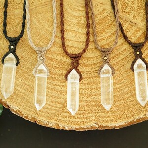May include: Five necklaces featuring clear, double-terminated quartz crystal points suspended from braided cords in black, beige, dark brown, light brown, and chocolate brown, each secured with a small metallic bead above the crystal.