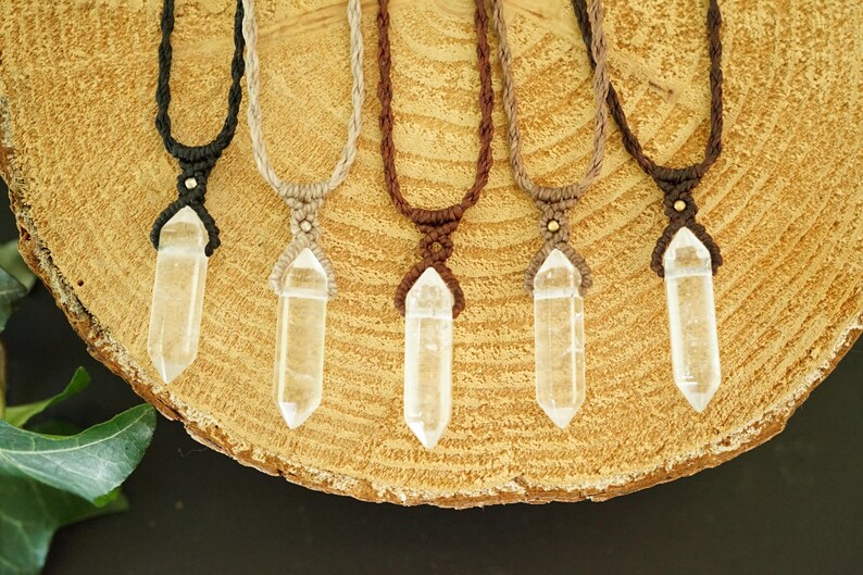 May include: Five necklaces featuring clear, double-terminated quartz crystal points suspended from braided cords in black, beige, dark brown, light brown, and chocolate brown, each secured with a small metallic bead above the crystal.