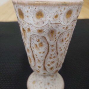 May include: A white ceramic goblet with a brown speckled glaze. The goblet has a wide, flared top and a round base.