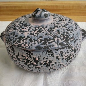May include: A ceramic casserole dish with a lid. The dish is round and has a speckled pink and black glaze. The lid has a knob on top.