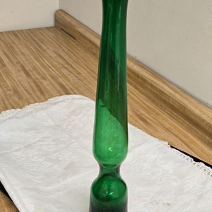 May include: A tall, green glass vase with a bulbous base. The vase is made of thick glass and has a smooth, glossy finish.