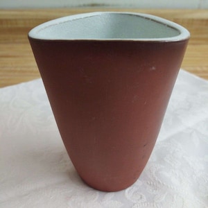 May include: A terracotta-colored ceramic planter with a white glazed interior. The planter has a rounded, triangular shape.