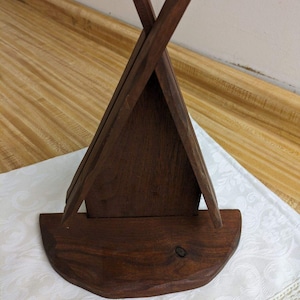 May include: A wooden teepee-shaped stand with a rounded base. The stand is made of dark brown wood and has a rustic appearance.