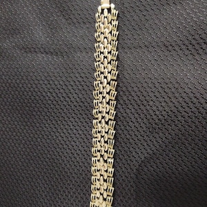 May include: A gold-tone bracelet with a chain-link design. The bracelet is made of small, oval-shaped links that are connected together to form a continuous chain.