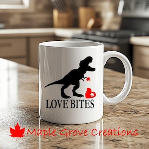 May include: White ceramic coffee mug with a black silhouette of a dinosaur biting a red heart with a puzzle piece missing. The text "LOVE BITES" is printed in black below the dinosaur.