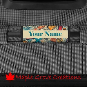 Op de afbeelding: Gepersonaliseerde bagagestrap met een vintage reiskaartontwerp. De strap heeft een blauw en wit vliegtuig, postzegels en de tekst "Your Name".