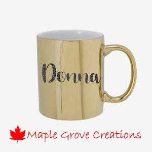 May include: Gold ceramic mug with a black glitter design that says "Donna".