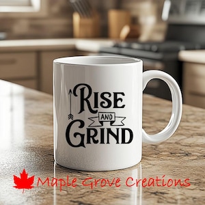 Può includere: Una tazza da caffè in ceramica bianca con una grafica nera che recita "Rise and Grind" con una freccia che punta verso l'alto.