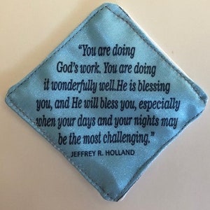 May include: A light blue diamond-shaped fabric pouch with a quote by Jeffrey R. Holland that reads, "You are doing God's work. You are doing it wonderfully well. He is blessing you, and He will bless you, especially when your days and your nights may be the most challenging."