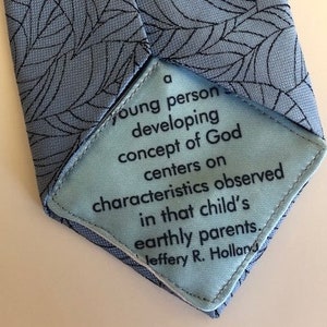 May include: A blue tie with a leaf pattern. The tie has a hidden message that reads: "A young person developing a concept of God centers on characteristics observed in that child's earthly parents. Jeffery R. Holland"