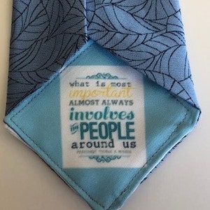 May include: A blue tie with a white leaf pattern. The tie has a small tag attached to it that says "what is most important almost always involves the people around us".