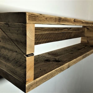 May include: A rustic wooden shelf with two shelves, made from reclaimed wood. The shelf is mounted to the wall and has a triangular design on the left side.